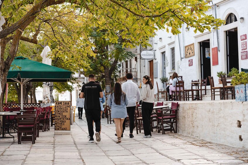 A street lined with outdoor cafes, a green umbrella, and a signboard with text. 5
