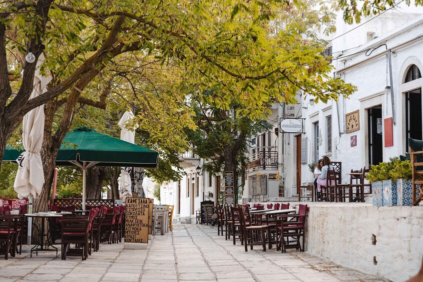 A street lined with outdoor seating, trees, and white buildings with signage. 2