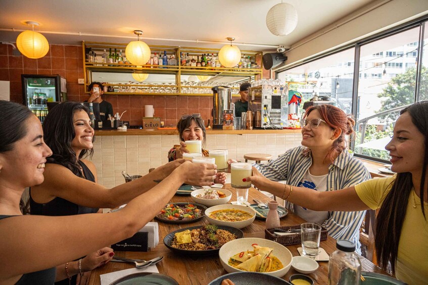 A group of people toasting with drinks at a restaurant with a bar area in the background. 1
