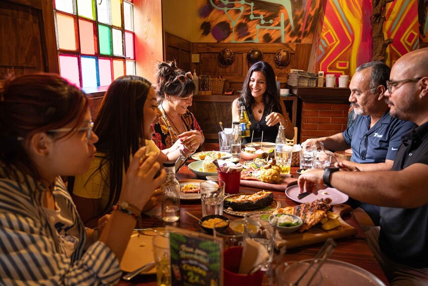 A group of people dining at a restaurant with a colorful mural and wooden decor. 2