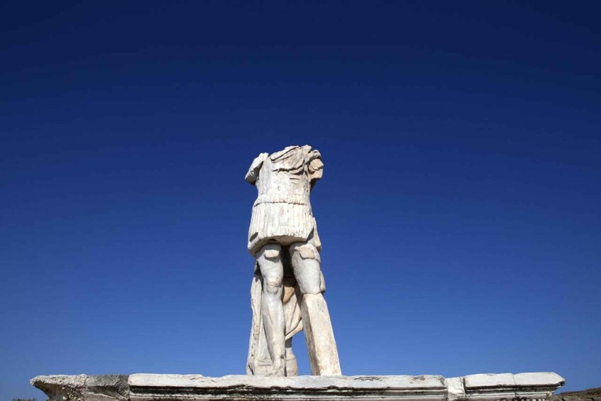 A white marble statue of a figure with a raised arm, standing on a pedestal against a clear blue sky. 1