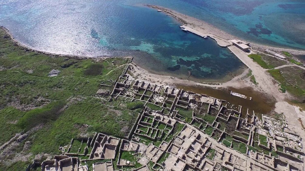 An aerial view of an ancient city with a coastal layout, featuring a grid of ruins and a narrow waterway connecting to the sea. 2