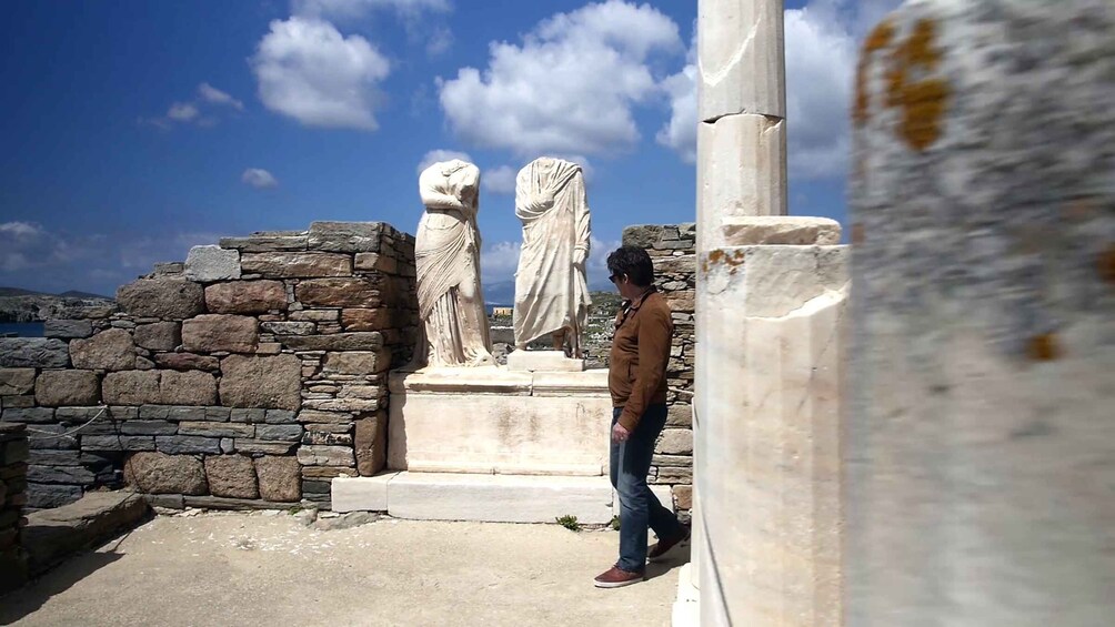 A man standing near ancient stone ruins with two classical statues. 5