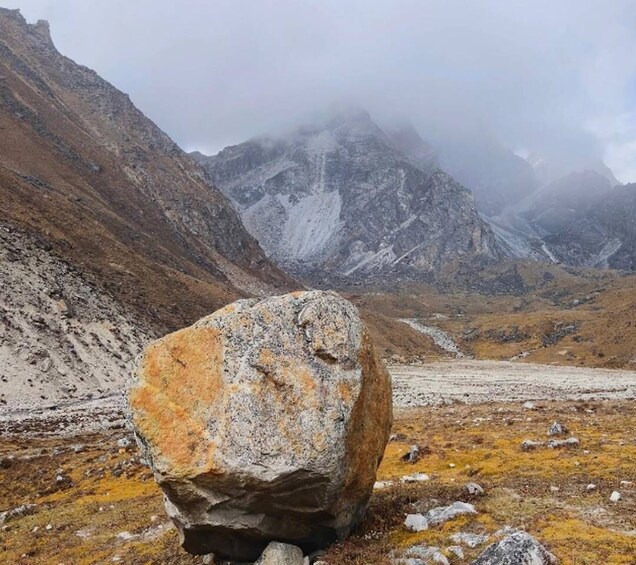 Un enorme bloque de piedra en un paisaje montañoso con picos nevados al fondo. 3