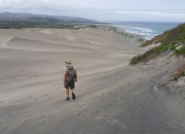 A person hiking on a sandy beach with ocean waves in the background. 2