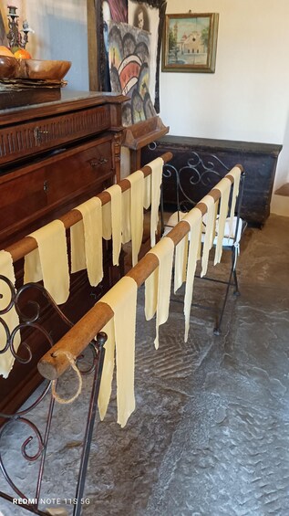 A drying rack with pasta hanging in a room with a wooden cabinet and a painting on the wall. 5
