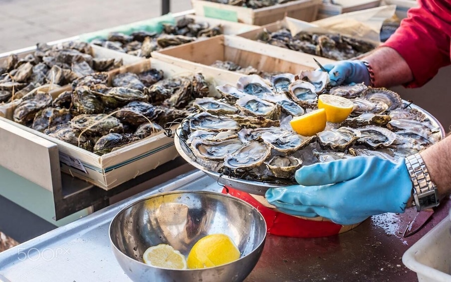 A person wearing gloves handling a tray of oysters with lemon wedges. 1
