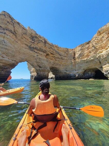 A person kayaking in clear waters with a natural rock arch formation in the background. 5