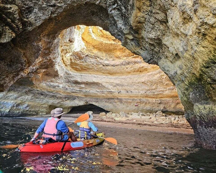 Two people kayaking in a cave with a large rock formation in the background. 1