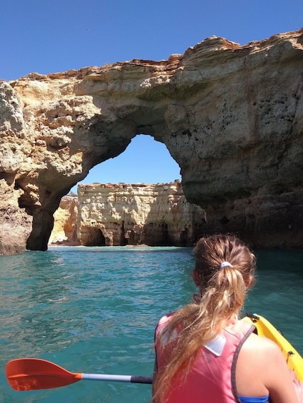 A kayaker paddling through a natural arch formation in clear waters. 3