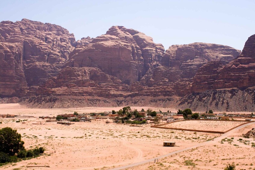 A desert landscape with rocky mountains in the background and a small settlement with sparse vegetation in the foreground. 2