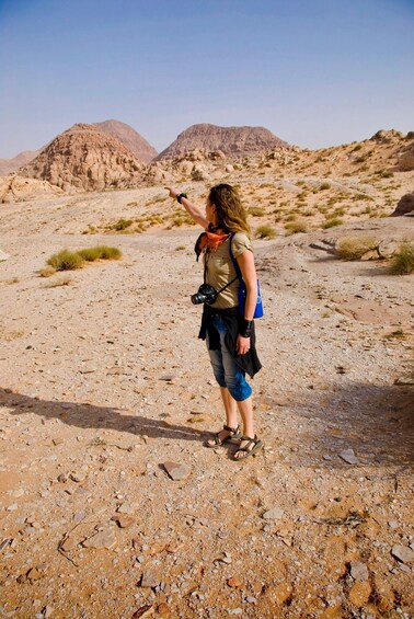 A person hiking in a rocky desert landscape with mountains in the background. 1