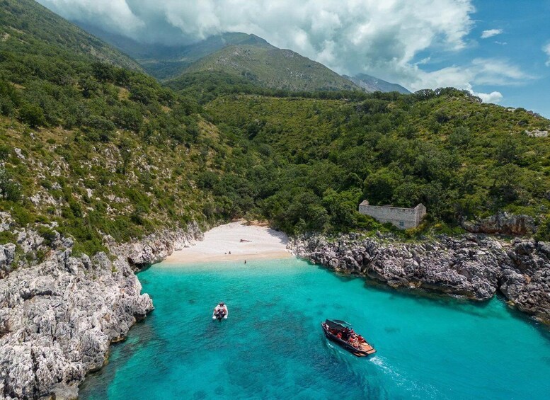 A turquoise bay with boats, a sandy beach, and a stone wall. 5