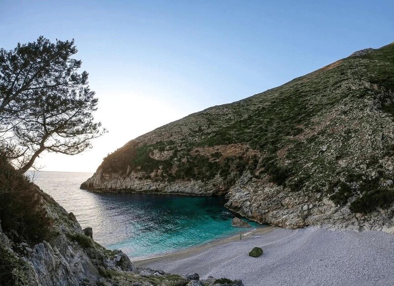 A coastal landscape with a rocky cliff, turquoise sea, and a sandy beach. 3