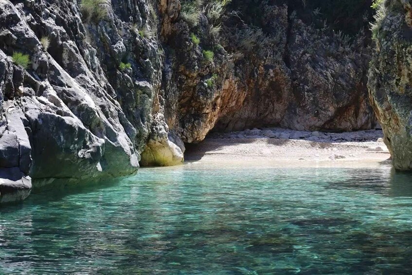 A clear turquoise pool surrounded by rocky cliffs and sparse vegetation. 4