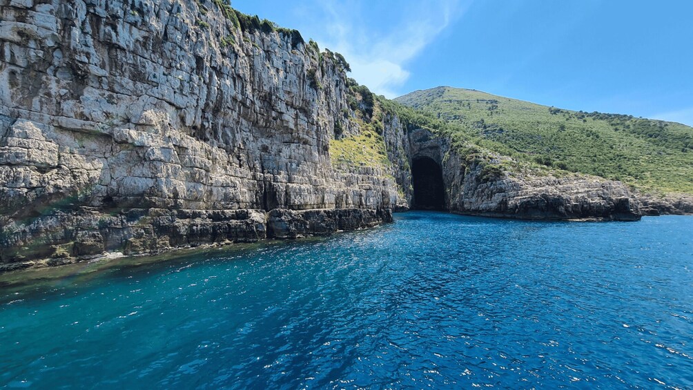A coastal cliff with a cave entrance and a clear blue sea. 1
