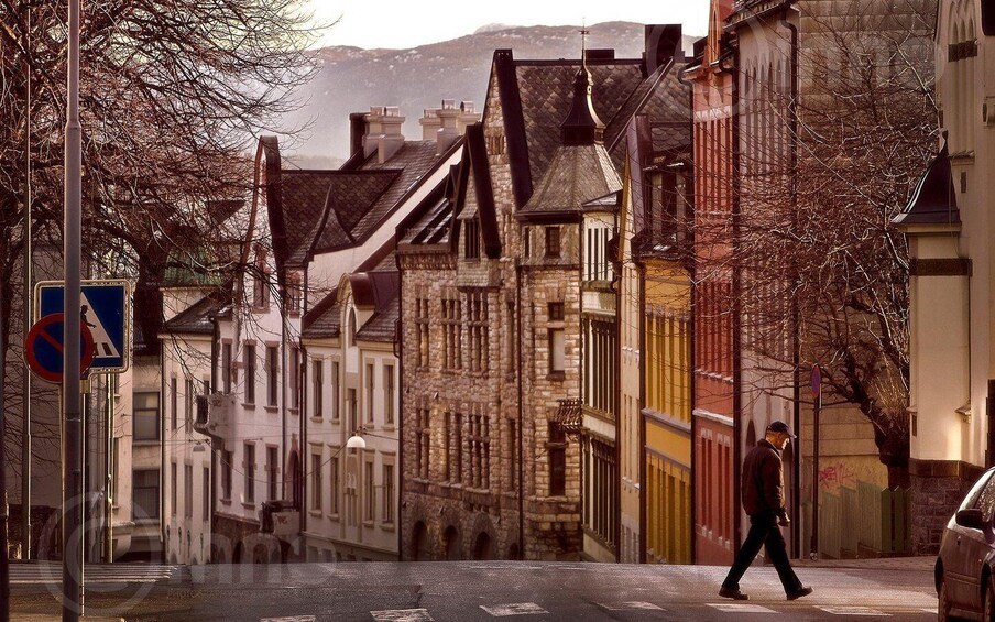 A pedestrian crossing a street with historic buildings, a no parking sign, and a clear sky. 2