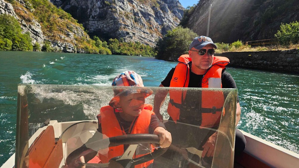 Two people in a boat on a river with rocky cliffs in the background. 4