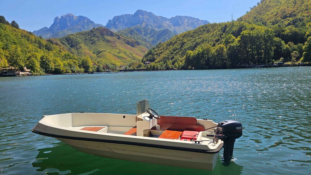 A small motorboat on a calm lake with a mountainous backdrop. 1