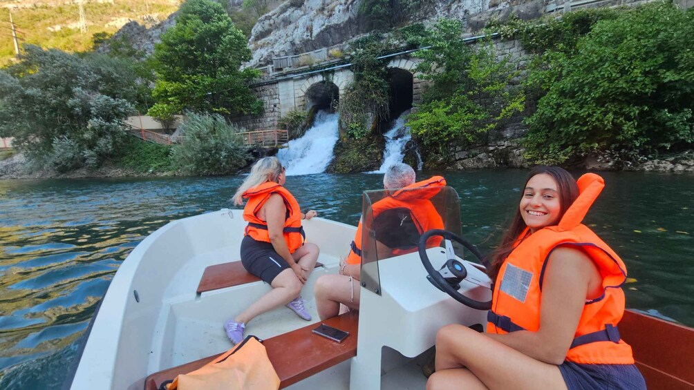 Two people on a boat wearing life jackets, with a waterfall in the background. 3