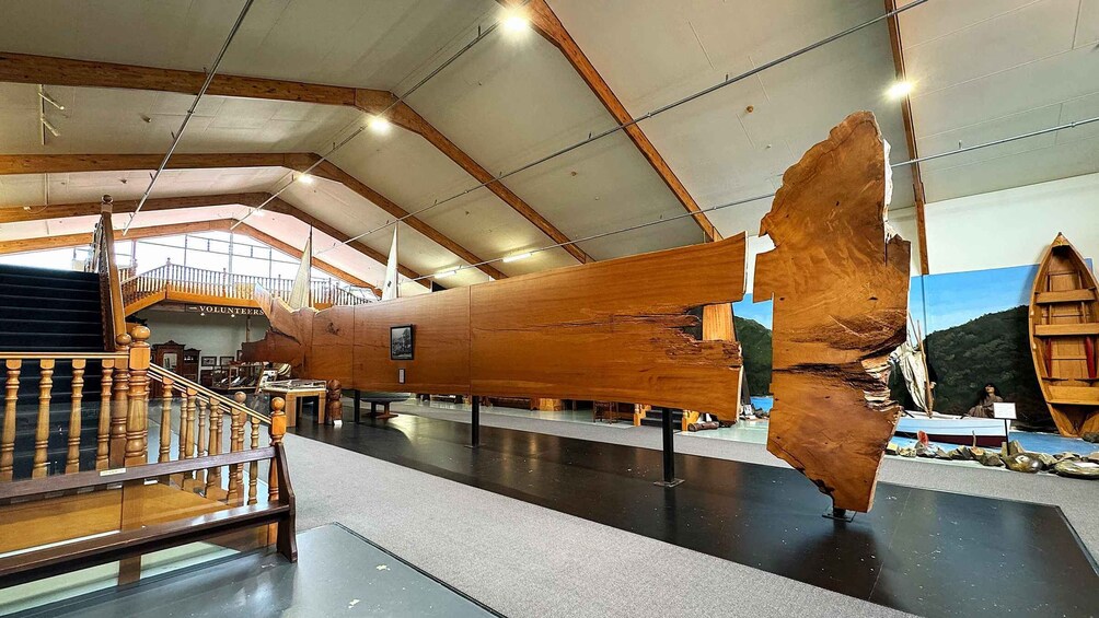 A large wooden ship model displayed indoors with a staircase and a mural in the background. 3