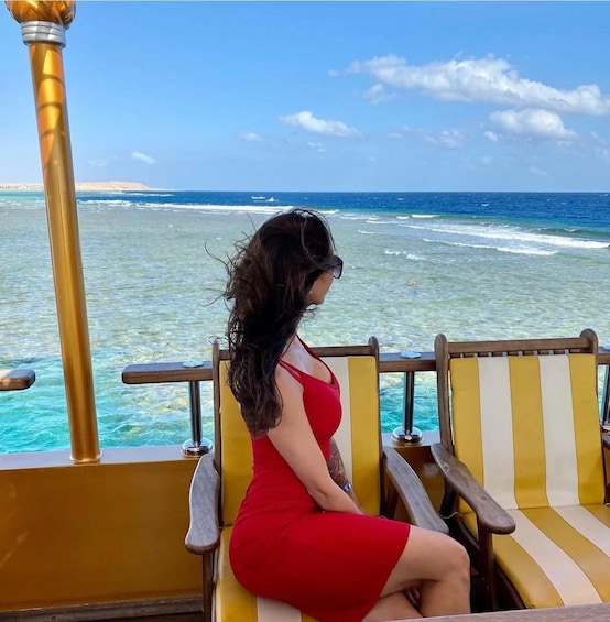 A person in a red dress sitting on a yellow and white striped chair, overlooking turquoise ocean waters. 5