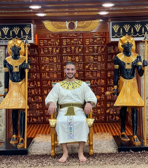 A person seated in front of a backdrop with Egyptian hieroglyphs and statues. 4