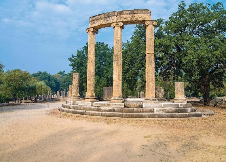 Columnas de piedra antiguas con base circular, rodeadas de árboles y cielo despejado. 1