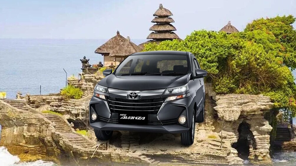 A Toyota New Grandia SUV parked on a rocky coastal area with traditional Balinese architecture in the background. 1