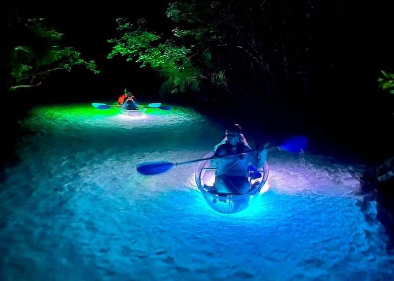 Two kayakers in a river at night, illuminated by blue lights. 1