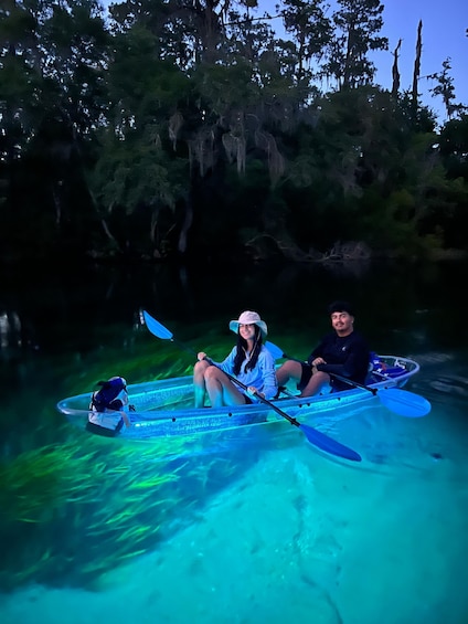 Two people kayaking in a clear blue water body surrounded by trees. 2