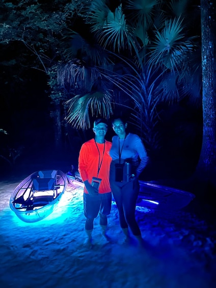Two people standing near a boat on a sandy beach at night, illuminated by blue lights. 3