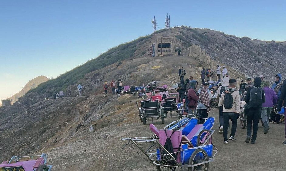 A group of people ascending a hill with carts and a building at the top. 5