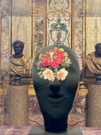 A sculpture of a human head with a floral design on top, set against a marble background with other sculptures. 5