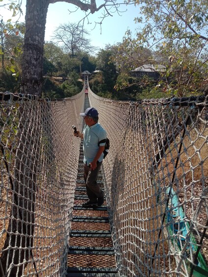 A man walking on a rope bridge surrounded by trees. 4