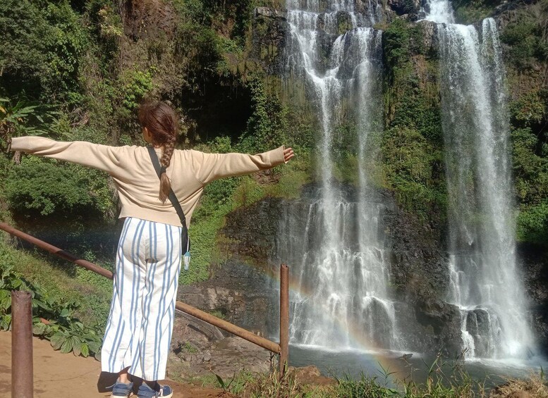 A person standing with arms outstretched in front of a multi-tiered waterfall. 1