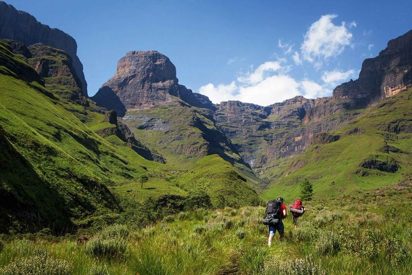 A hiker with a backpack walking through a lush green valley with steep cliffs. 5