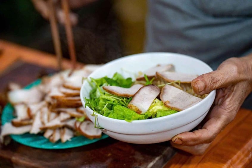 A bowl of salad with lettuce and sliced meat, held by a person. 4