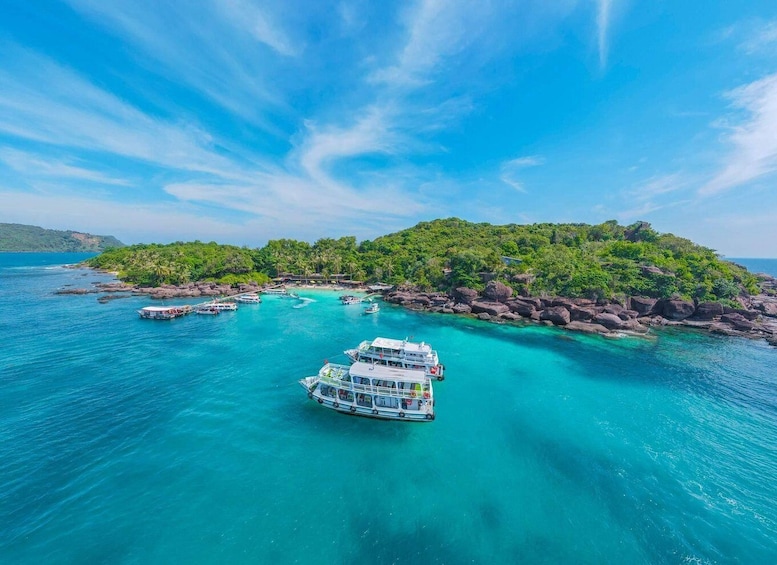 A boat in turquoise waters near a rocky island with lush greenery. 2