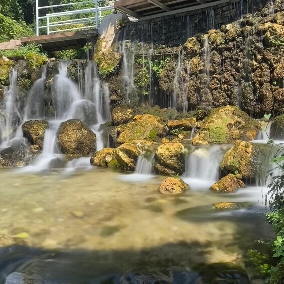 A waterfall cascading over moss-covered rocks with a wooden bridge in the background. 2