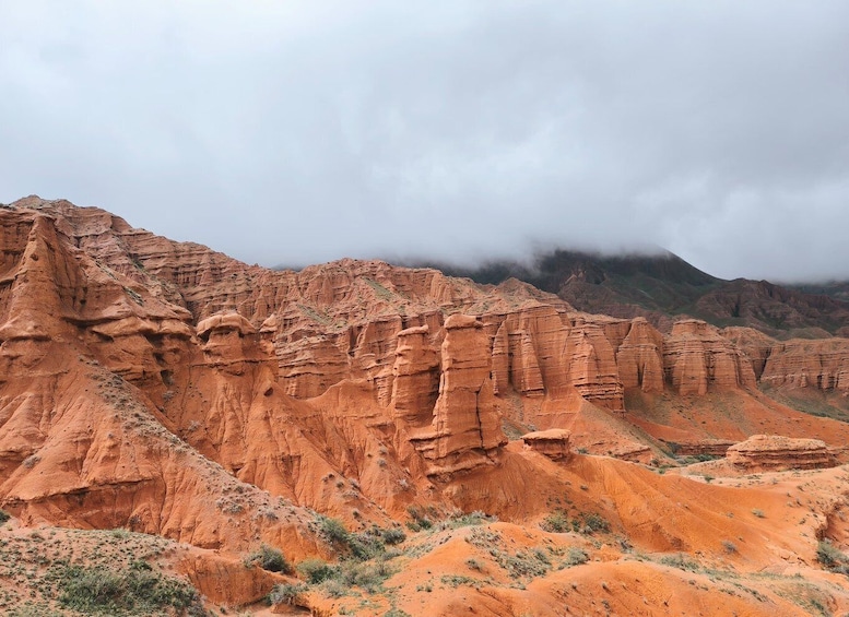 A rugged desert landscape with layered red rock formations and sparse vegetation. 1