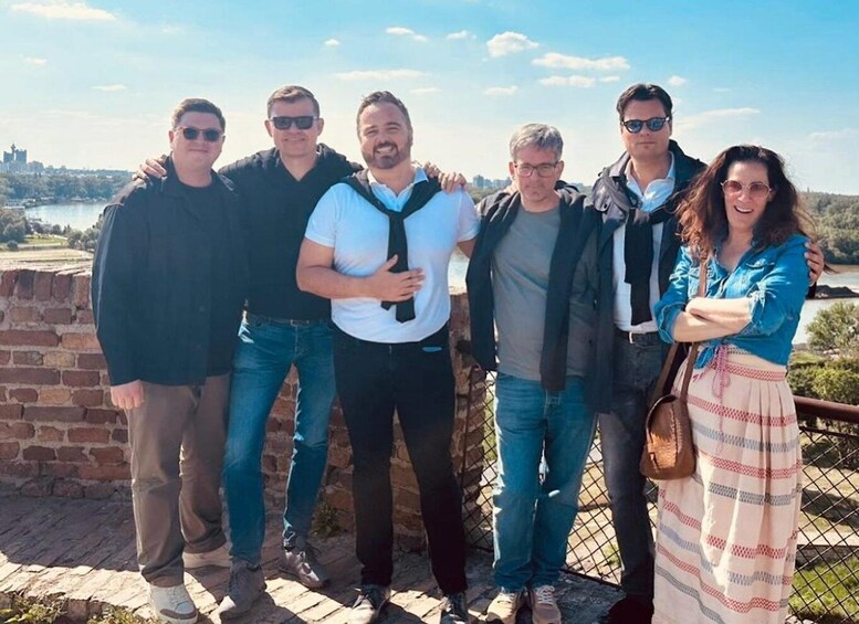A group of people standing by a brick wall with a scenic view of a lake and hills in the background. 5