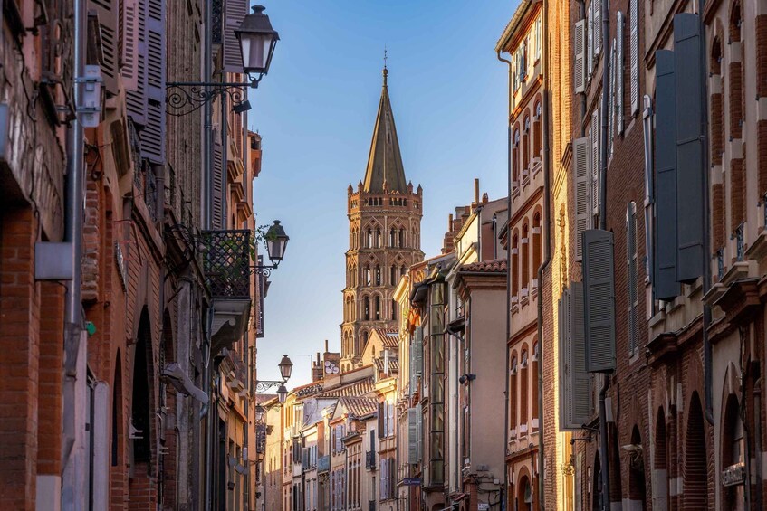 A narrow street lined with historic buildings and a prominent church tower. 3