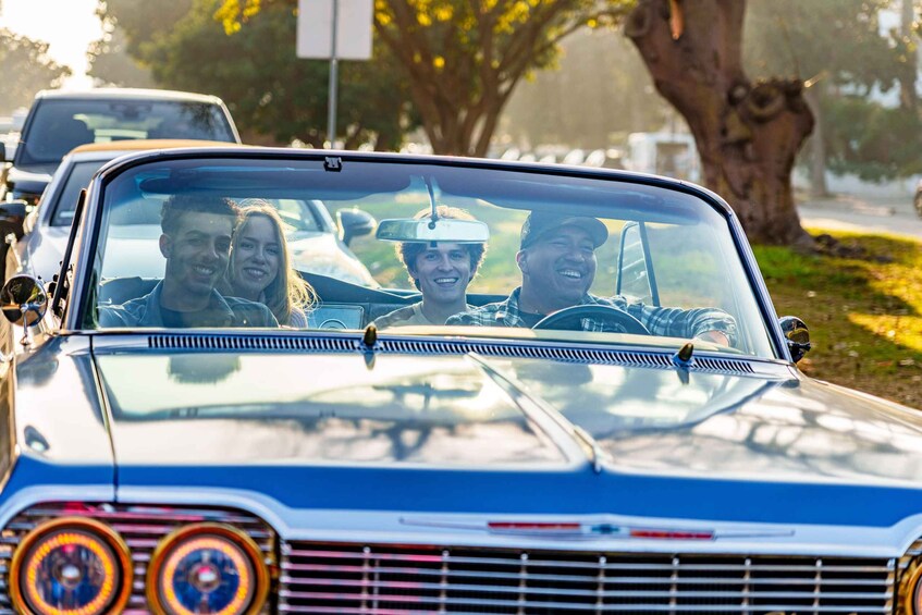 A vintage car with a distinctive grille and round headlights driving on a road. 3