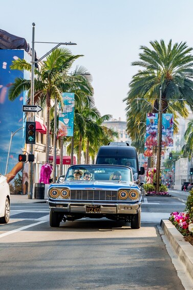 A vintage car with custom headlights driving on a city street lined with palm trees and colorful billboards. 4