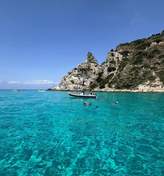 A clear turquoise sea with a rocky coastline, a boat with people, and a clear sky. 2