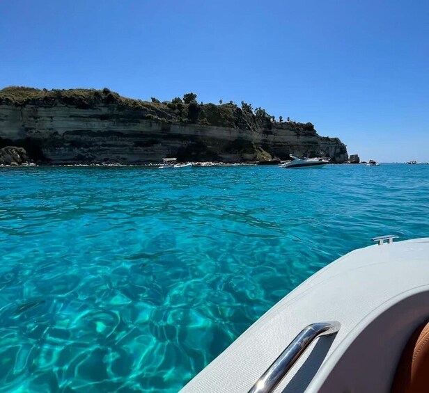A boat on clear turquoise water with a rocky coastline in the background. 5