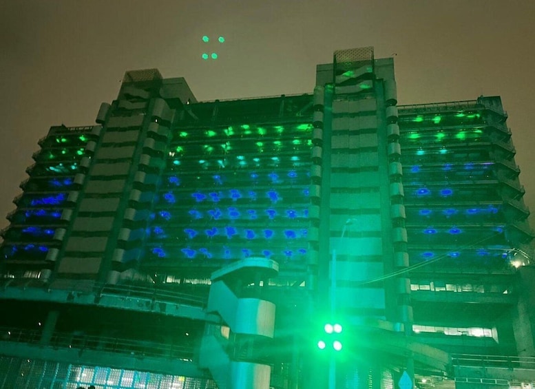 A multi-story building with illuminated windows in green and blue. 3