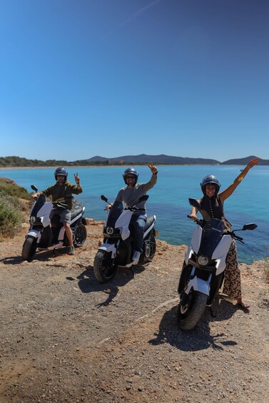 Three people on scooters by a lake with mountains in the background. 3