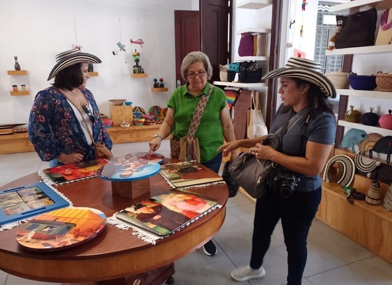 Three people examining colorful artworks at a round table in a shop. 3